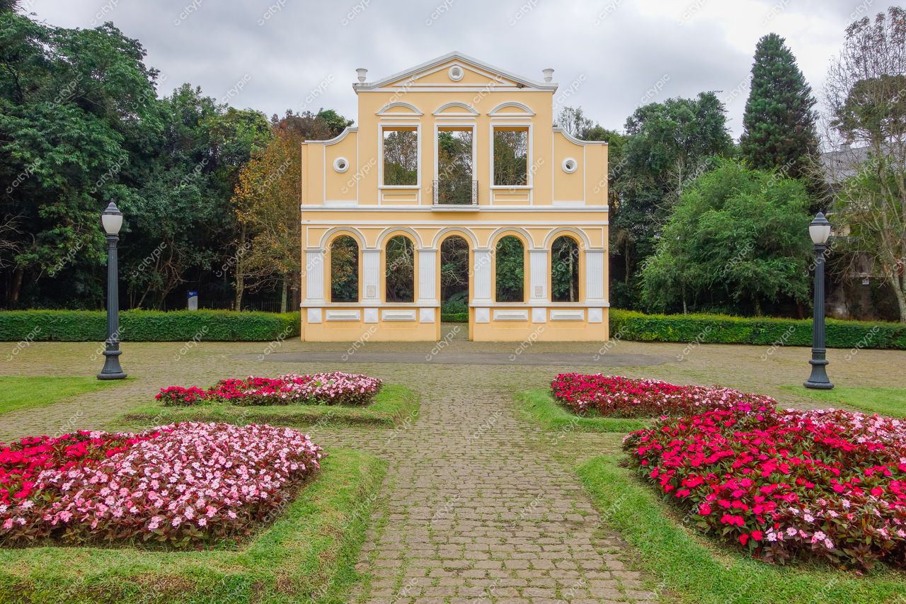 Curitiba, Paraná, construção histórica amarela com caminho de pedras e flores rosa e brancas em dia nublado