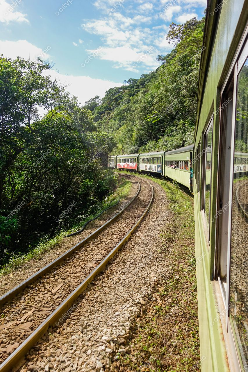 Morretes, Paraná, trem de cores claras em curva ferroviária cercada por vegetação da mata atlântica e relevo montanhoso