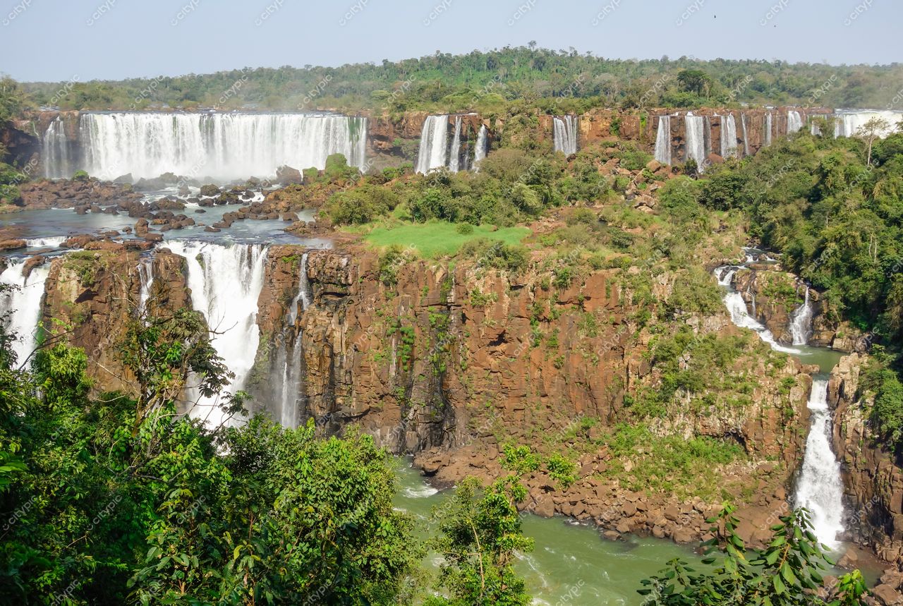 Foz do Iguaçu, Paraná, vista das Cataratas com luz do sol refletindo no rio e vegetação abundante ao redor