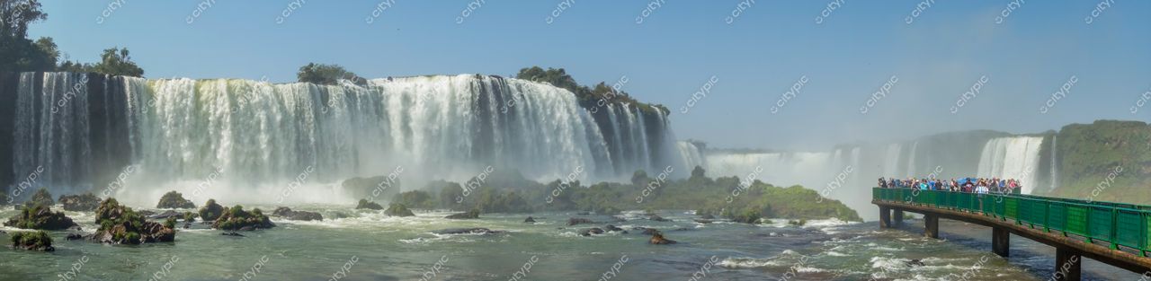 Foz do Iguaçu, Paraná, visitantes na passarela de madeira observam as quedas d’água sob luz clara do dia