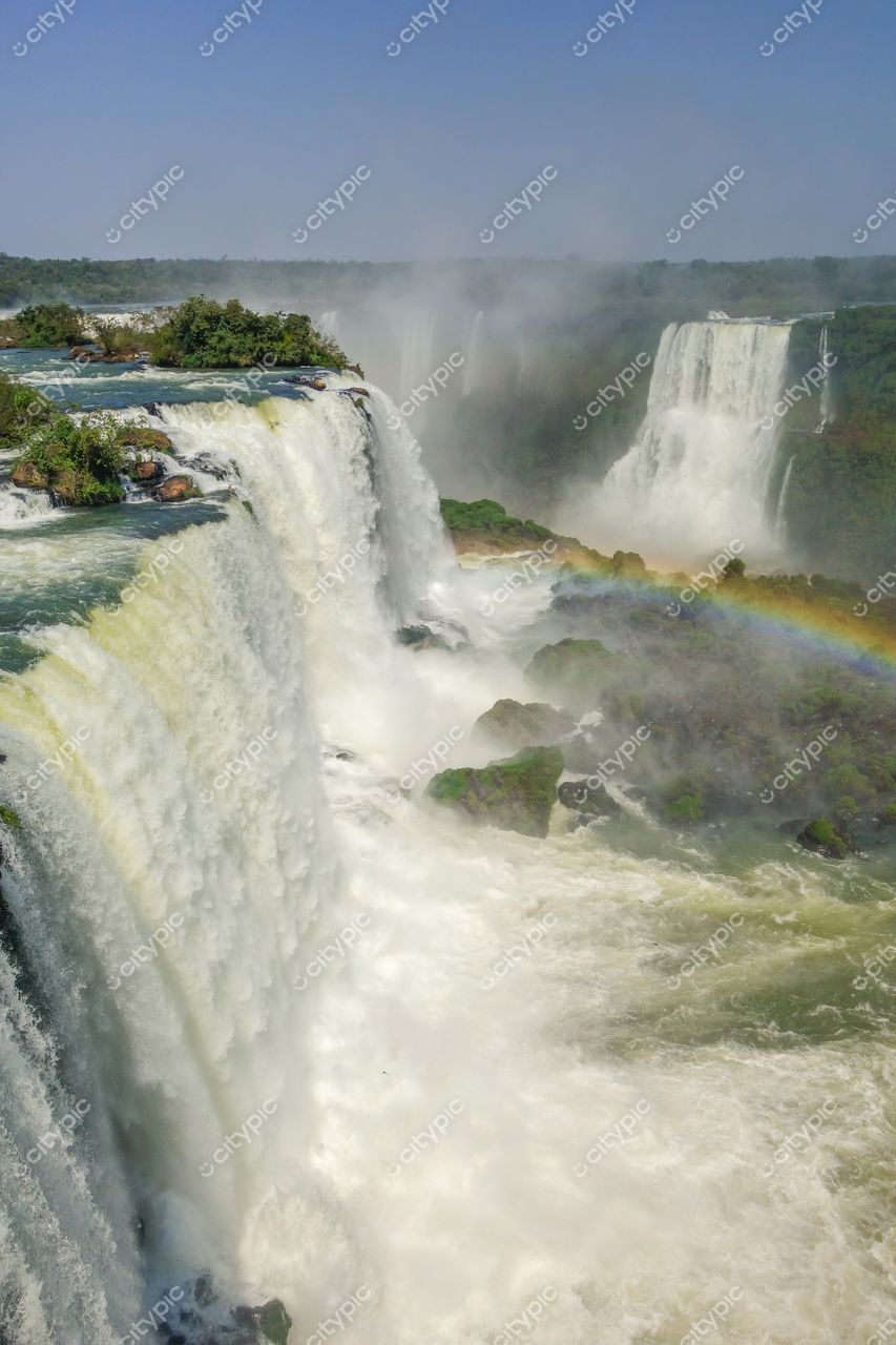 Foz do Iguaçu, Paraná, vista das Cataratas com névoa e arco-íris sob céu claro e vegetação densa