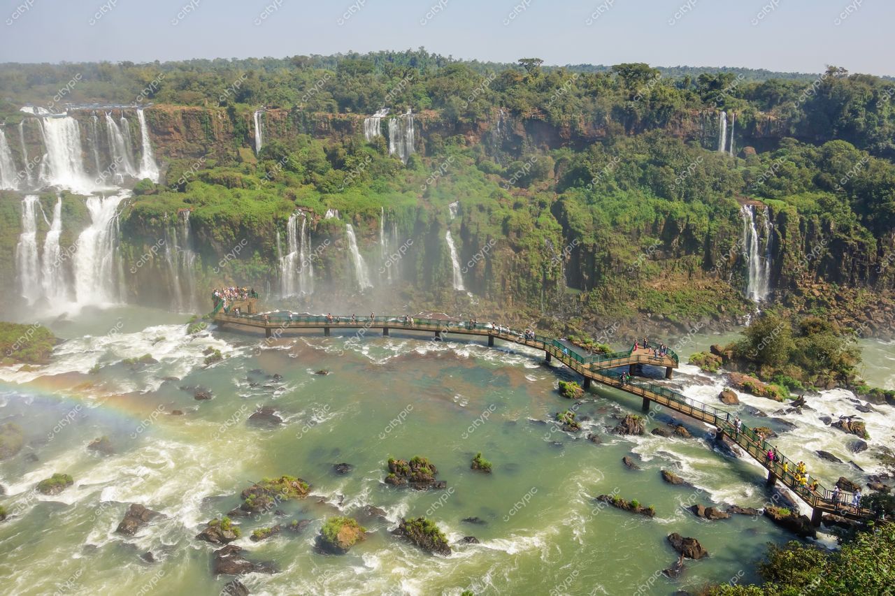 Foz do Iguaçu, Paraná, passarela de madeira em primeiro plano com vegetação verdejante e céu azul claro ao fundo