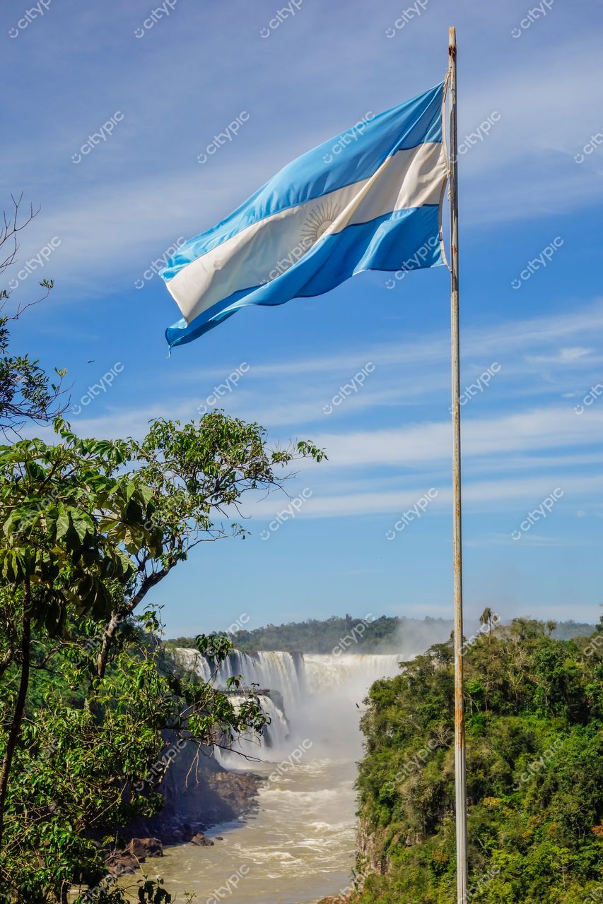 Foz do Iguaçu, Paraná, bandeira da Argentina em primeiro plano com Cataratas e vegetação sob céu parcialmente nublado