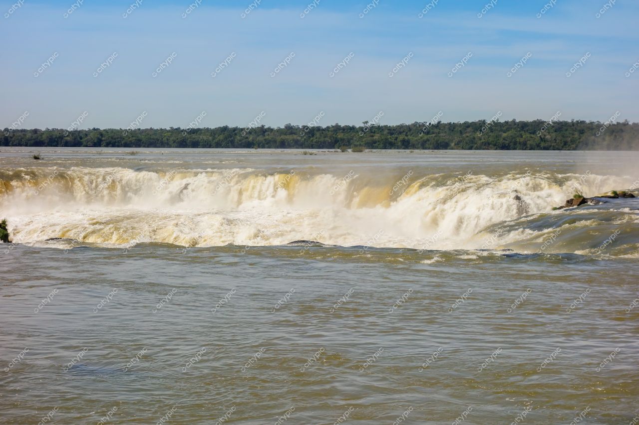 Foz do Iguaçu, Paraná, Cataratas com forte fluxo de água e vegetação densa sob céu azul claro