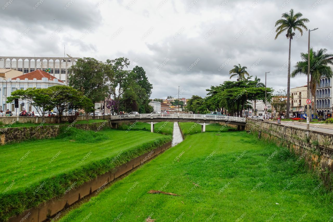 São João del Rei, Minas Gerais, vista urbana em dia nublado com canal, ponte branca e vegetação densa