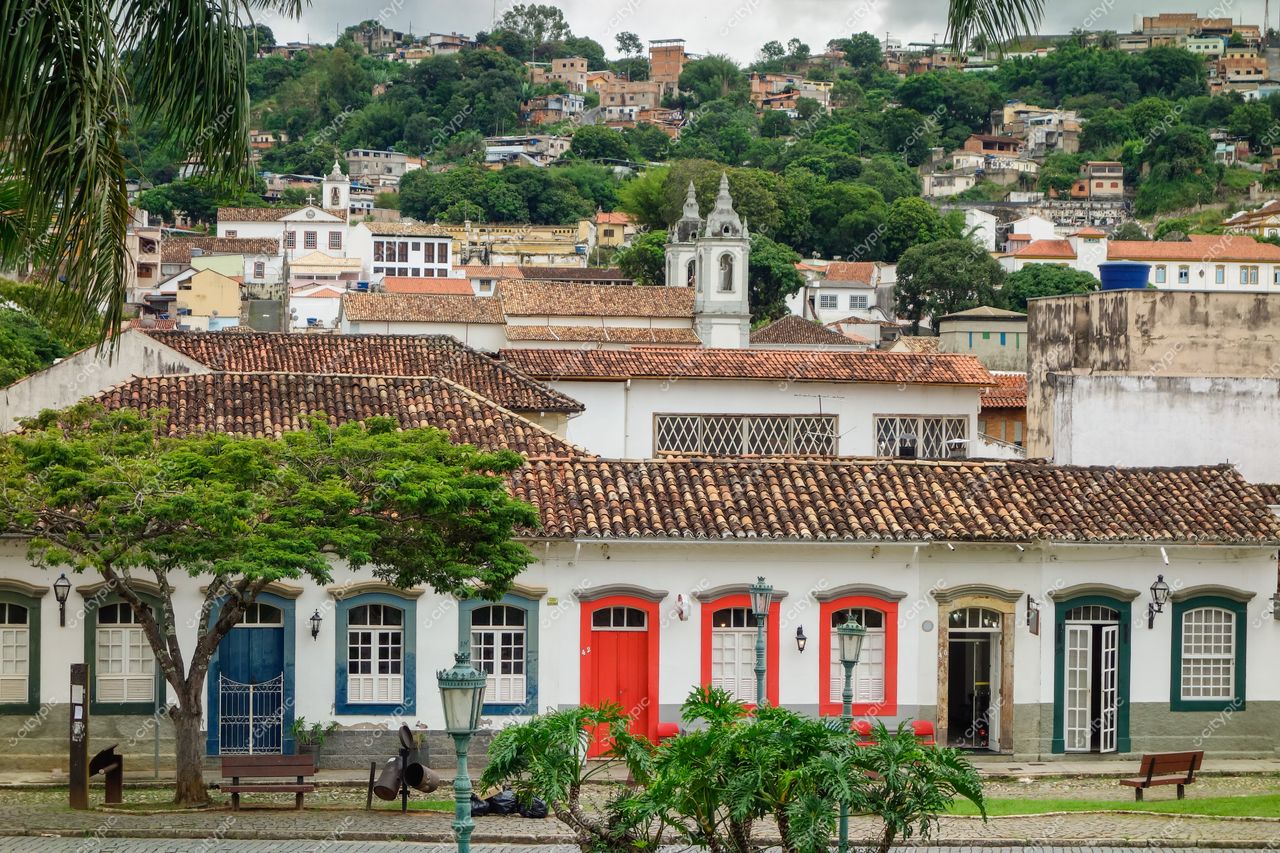 São João del Rei, Minas Gerais, casas coloniais em tons de branco e azul sob céu nublado com vegetação ao redor