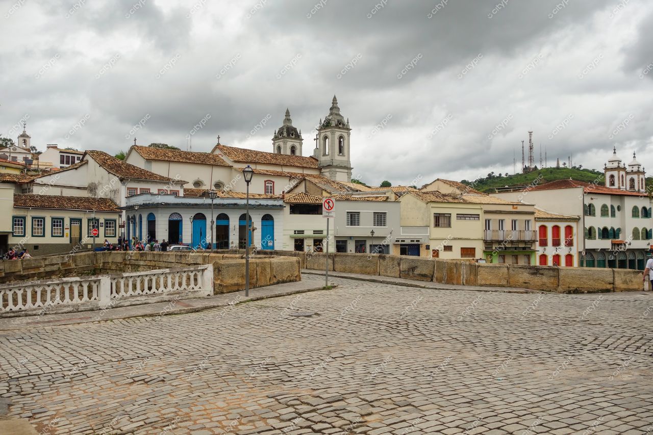 São João del Rei, Minas Gerais, céu nublado sobre rua de pedra com edifícios históricos e pessoas caminhando