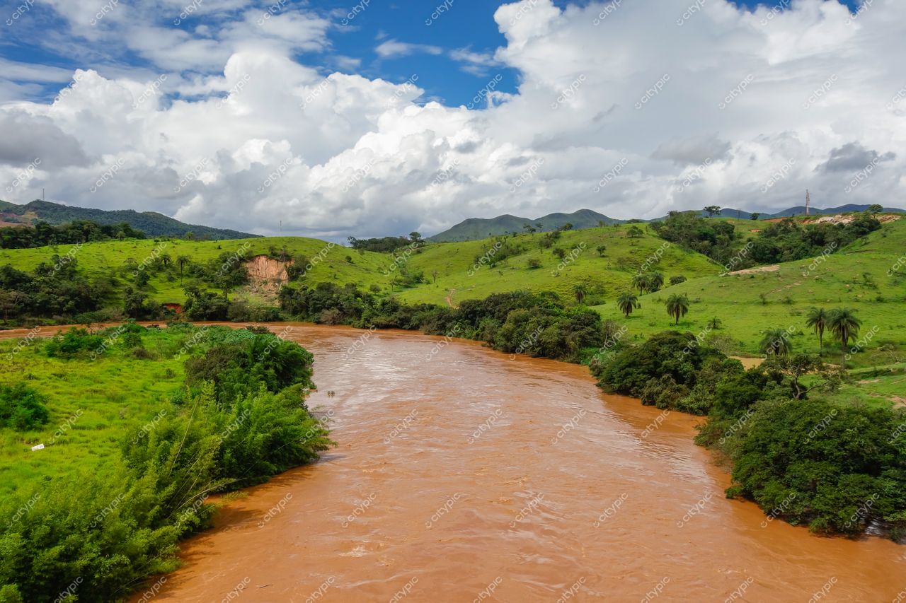 Brumadinho, Minas Gerais, rio de águas turvas em paisagem verde com colinas suaves e céu parcialmente nublado