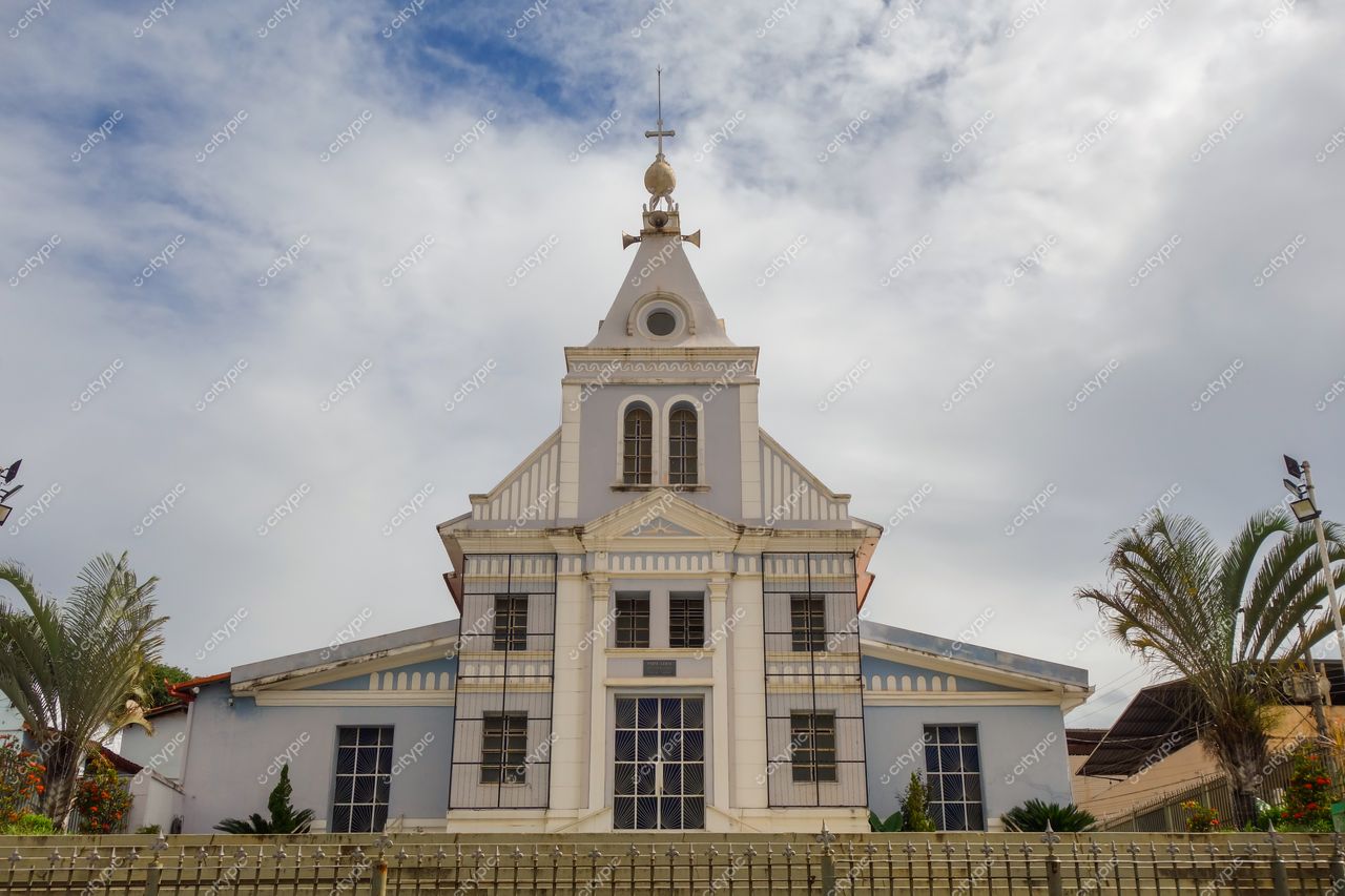 Brumadinho, Minas Gerais, igreja branca com detalhes azuis sob céu nublado e vegetação ao redor em ambiente urbano calmo