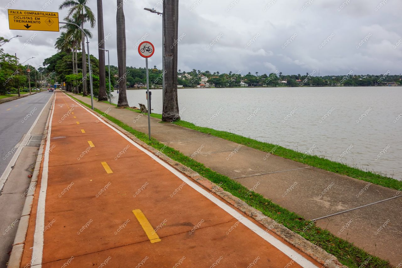 Belo Horizonte, Minas Gerais ciclovia compartilhada à beira do lago com piso laranja e vegetação ao fundo em dia nublado