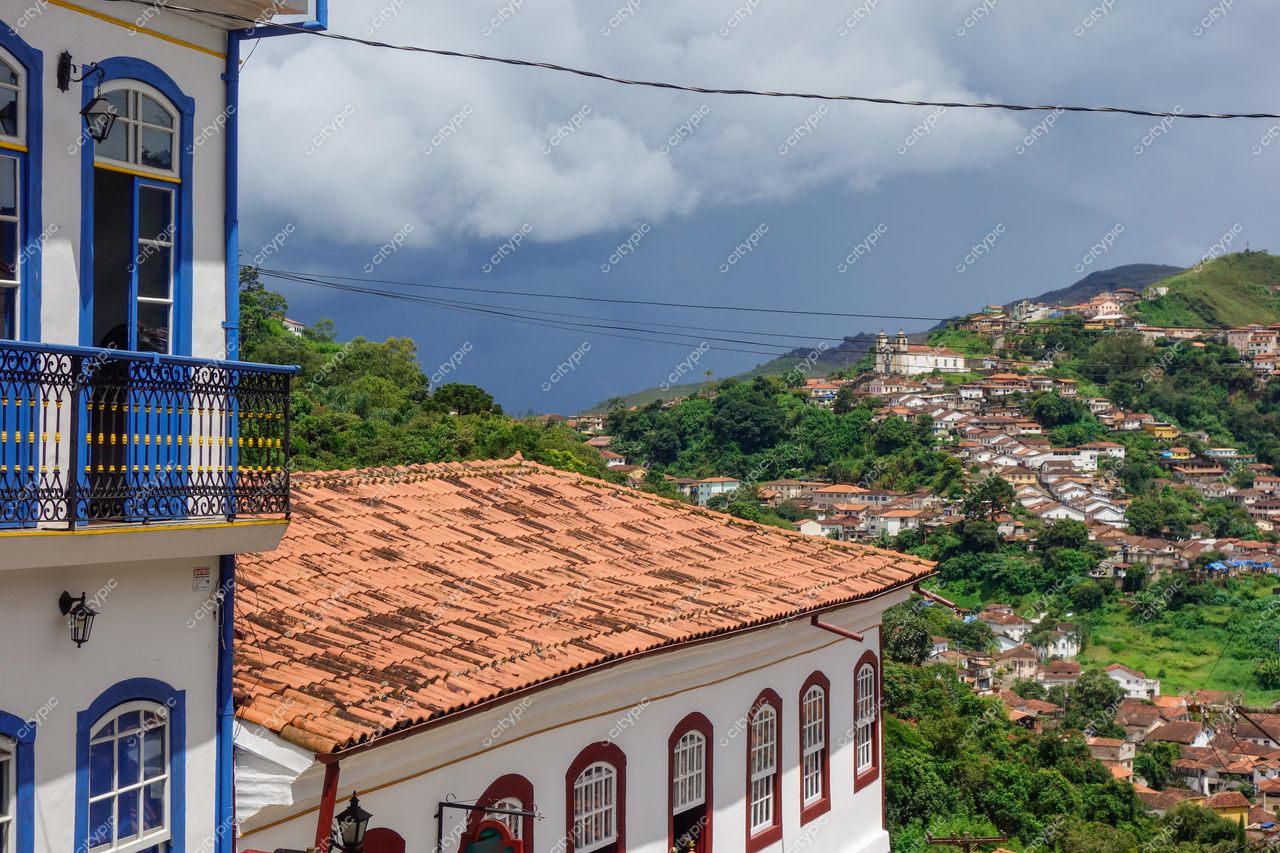 Ouro Preto, Minas Gerais, vista panorâmica com arquitetura colonial em azul e branco sob céu nublado e vegetação montanhosa