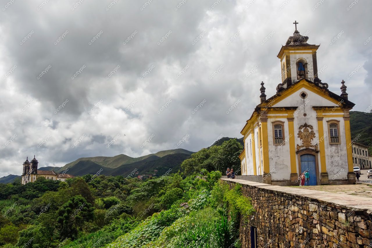 Ouro Preto, Minas Gerais vista com igreja branca e detalhes amarelos sob céu nublado e vegetação montanhosa ao fundo
