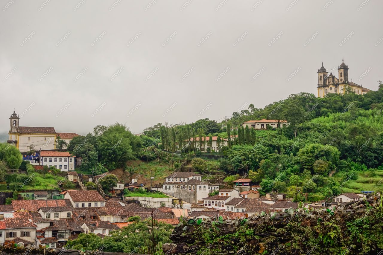 Ouro Preto, Minas Gerais com arquitetura colonial e céu nublado, destacando serras e vegetação densa ao fundo