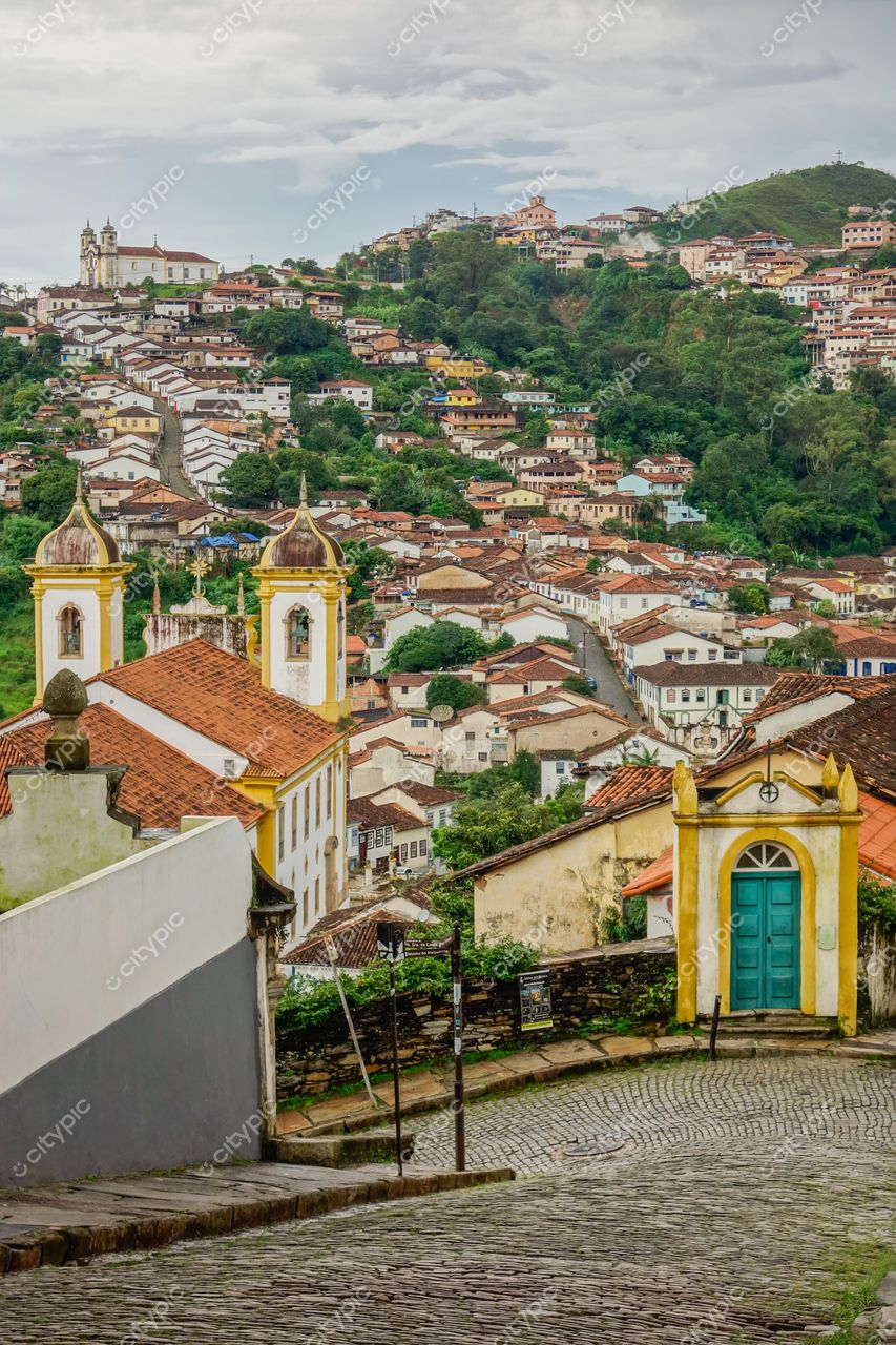 Ouro Preto, Minas Gerais vista panorâmica com torres de igreja e calçamento em pedra sob céu nublado e vegetação