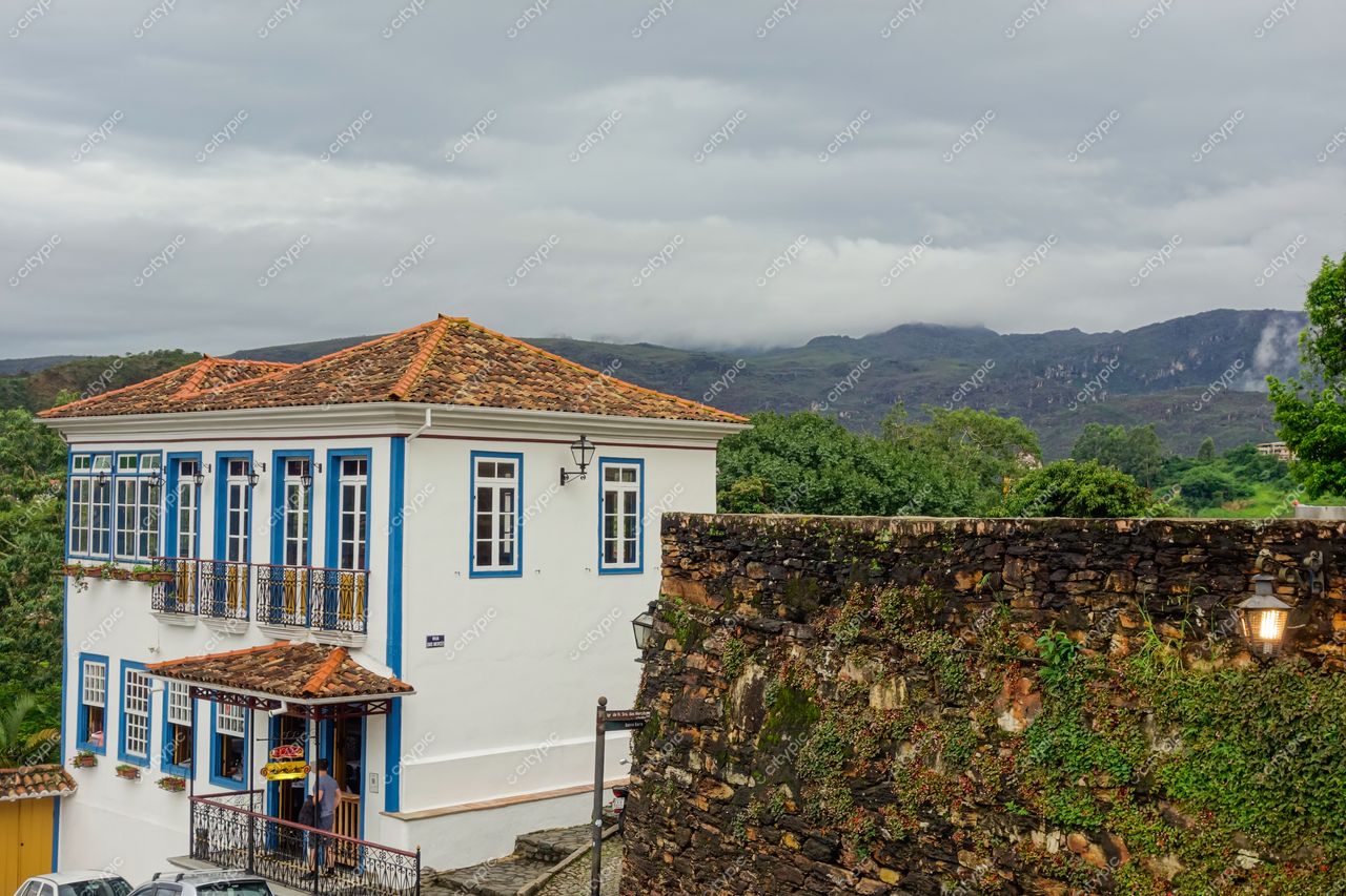 Ouro Preto, Minas Gerais, edifício colonial com janelões azuis e varanda de ferro em dia nublado e montanhas ao fundo