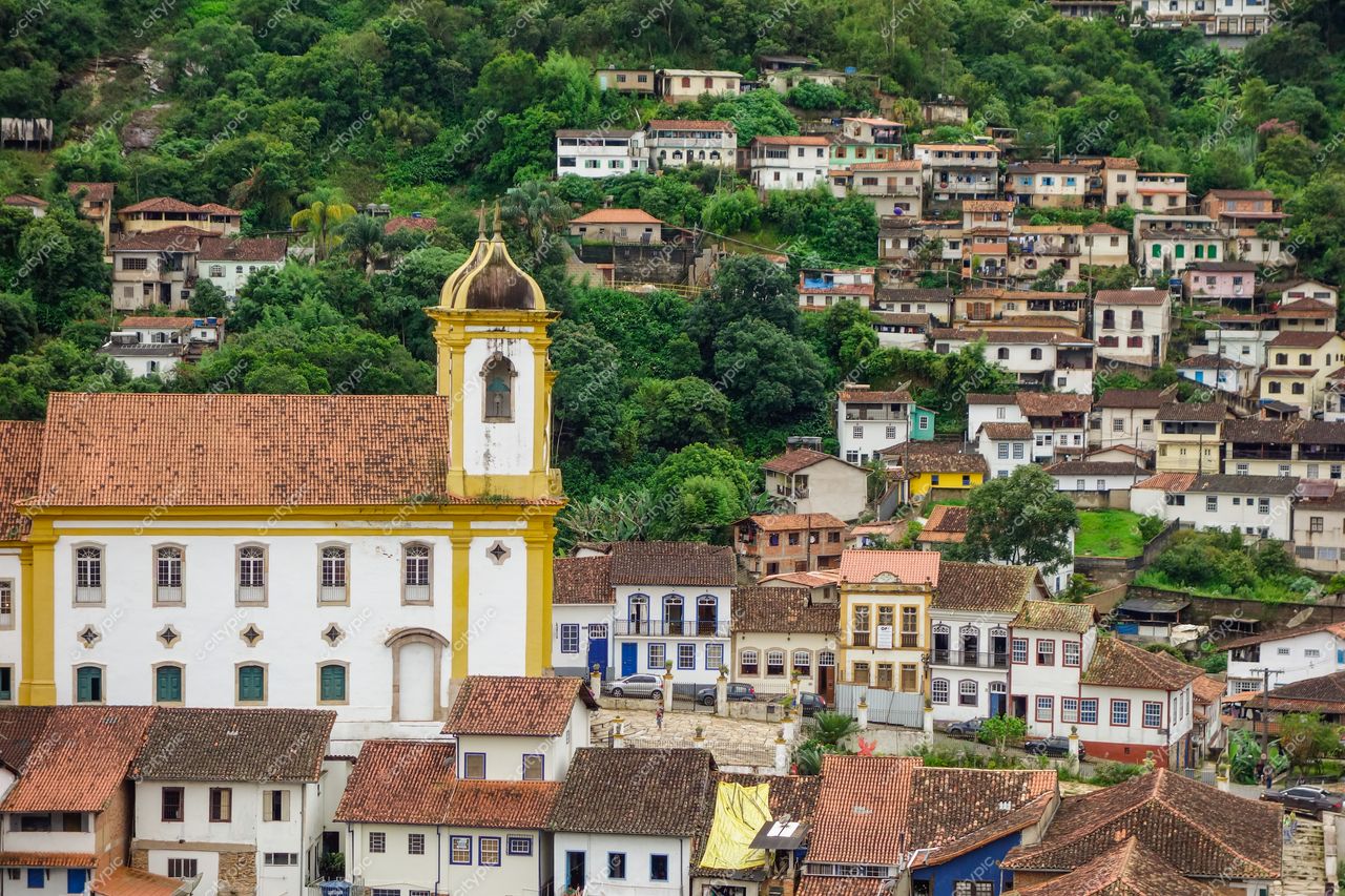 Ouro Preto, Minas Gerais com igreja amarela em primeiro plano e casas coloniais nas encostas verdes sob céu nublado