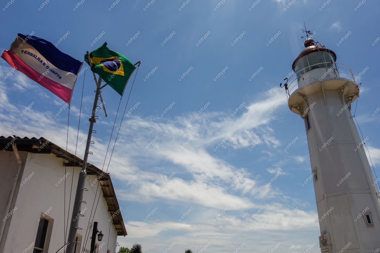 Vila Velha, Espírito Santo, farol branco com detalhes vermelhos sob céu azul e bandeiras hasteadas ao lado