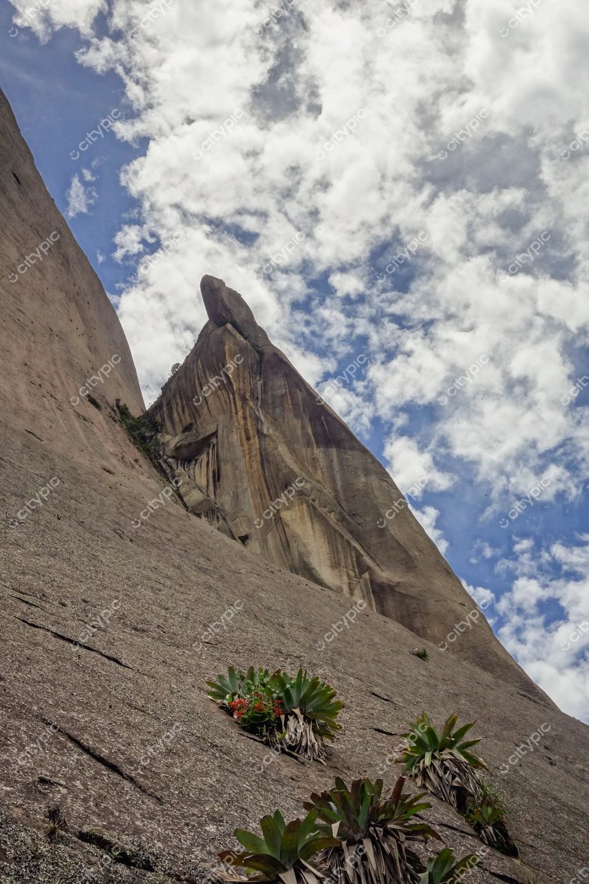 Domingos Martins, Espírito Santo, vista ascendente da formação rochosa com vegetação rasteira e céu parcialmente nublado