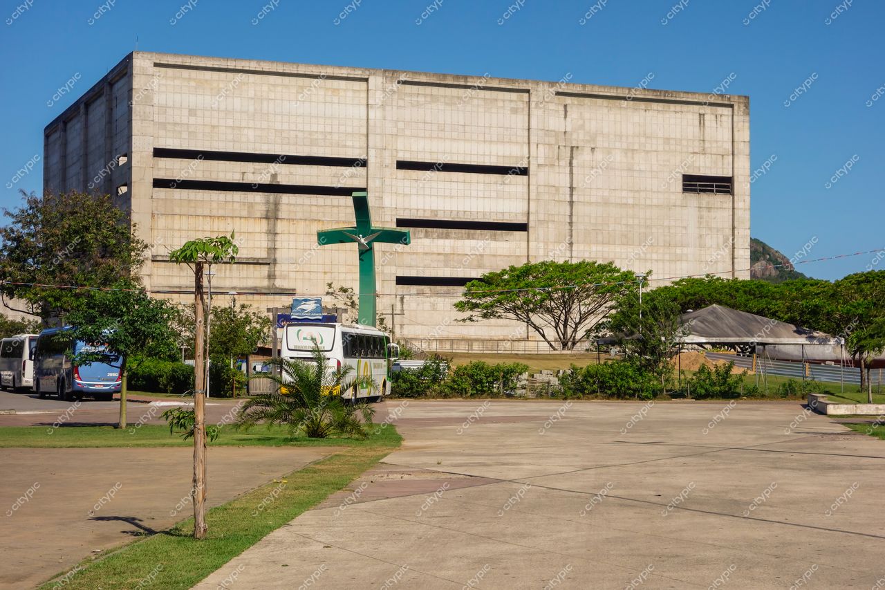 Vitória, Espírito Santo com edifício de concreto simples e cruz verde em dia ensolarado com vegetação e ônibus próximos