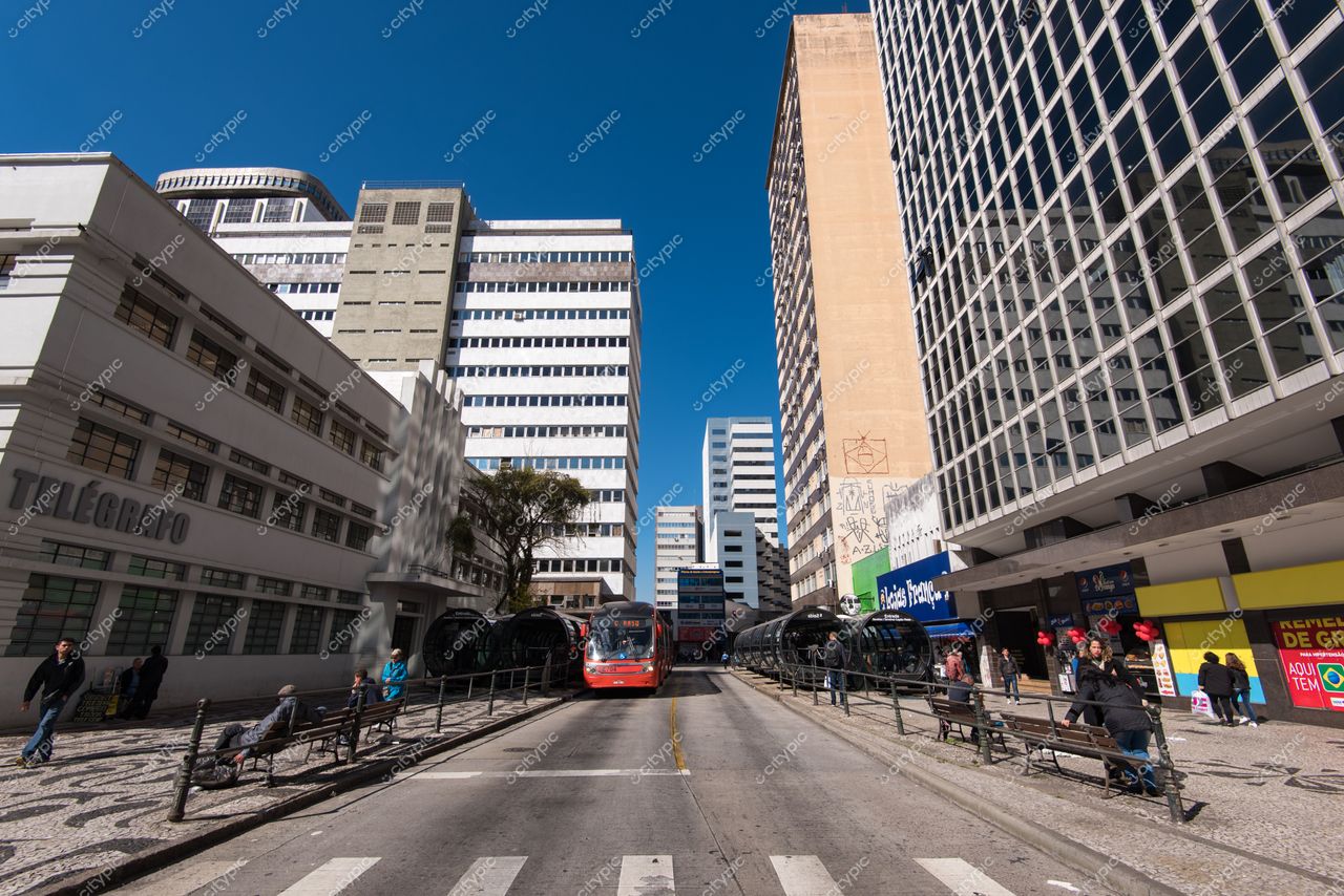 Curitiba, Paraná vista de rua com ônibus vermelho estacionado e pedestres em calçadas sob céu claro e iluminação diurna