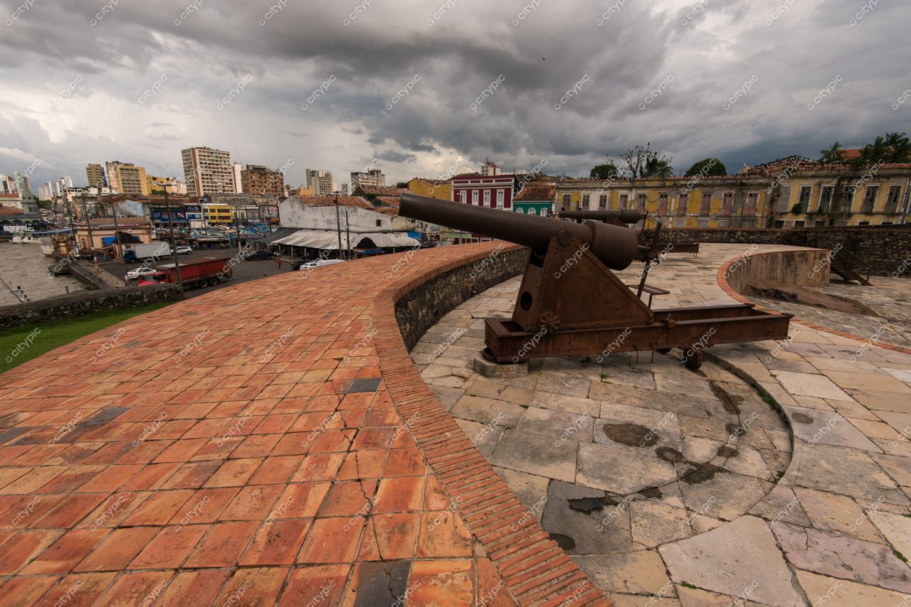 Belém, Pará, canhão de ferro em primeiro plano com edificações modernas e históricas sob céu nublado