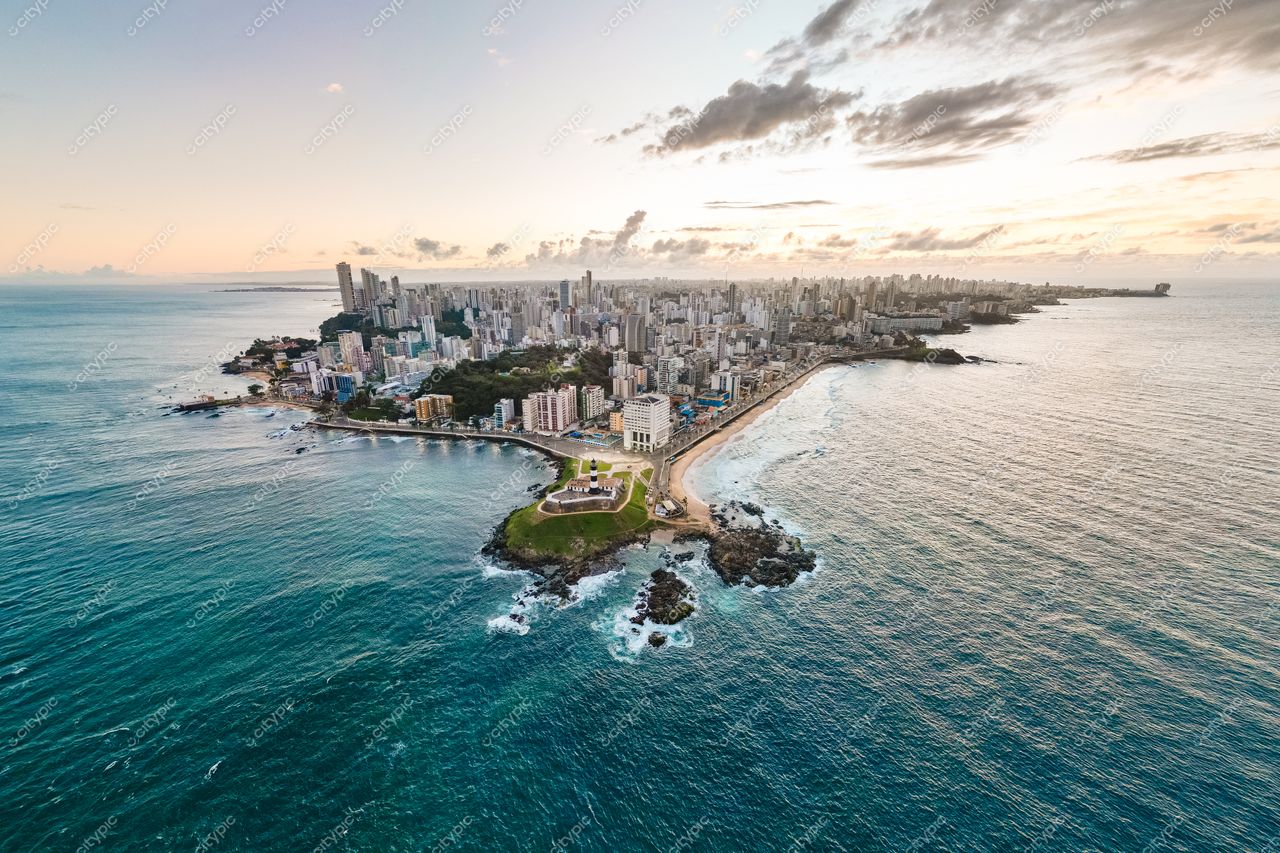 Salvador, Bahia vista aérea com edificações modernas, áreas verdes e mar em tonalidades de azul ao entardecer