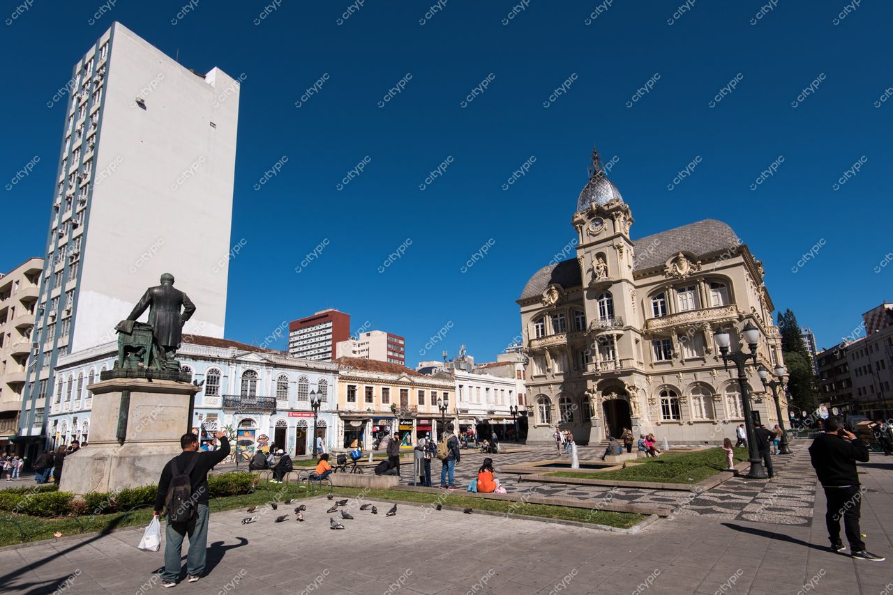 Curitiba, Paraná vista da praça central com monumento, pessoas e aves em dia ensolarado e céu azul