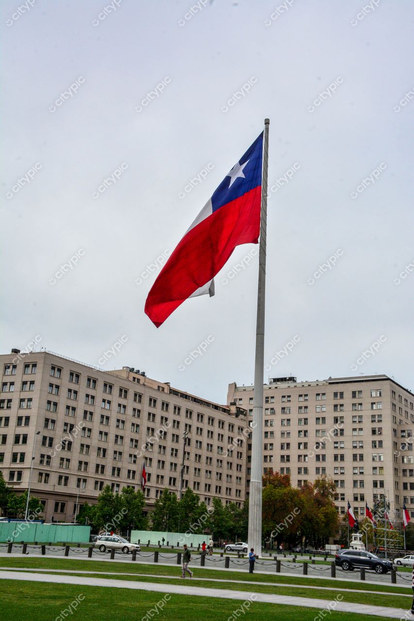 Plaza de la Ciudadanía, Santiago com bandeira do Chile em mastro sob céu nublado e arquitetura contemporânea ao fundo