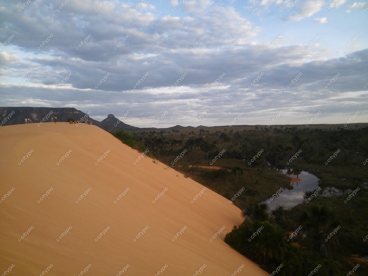 Jalapão, Tocantins, dunas de areia amarelada sob céu nublado com pessoas no topo e vegetação rasteira ao fundo