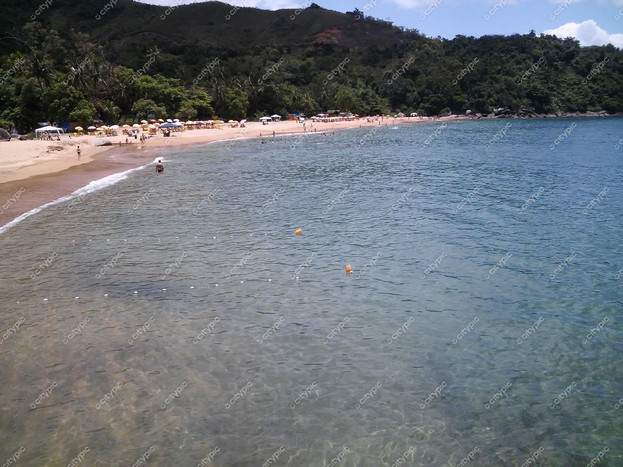 Ilhabela, São Paulo em dia ensolarado com praia de areia clara, água cristalina e vegetação montanhosa ao fundo