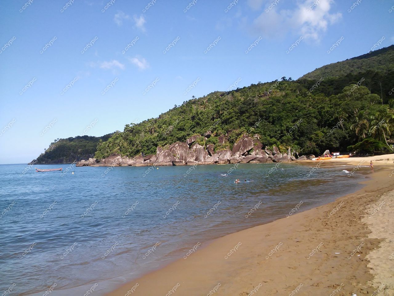 Ilhabela, São Paulo com praia tranquila e mar calmo refletindo céu azul em tarde ensolarada com vegetação ao fundo