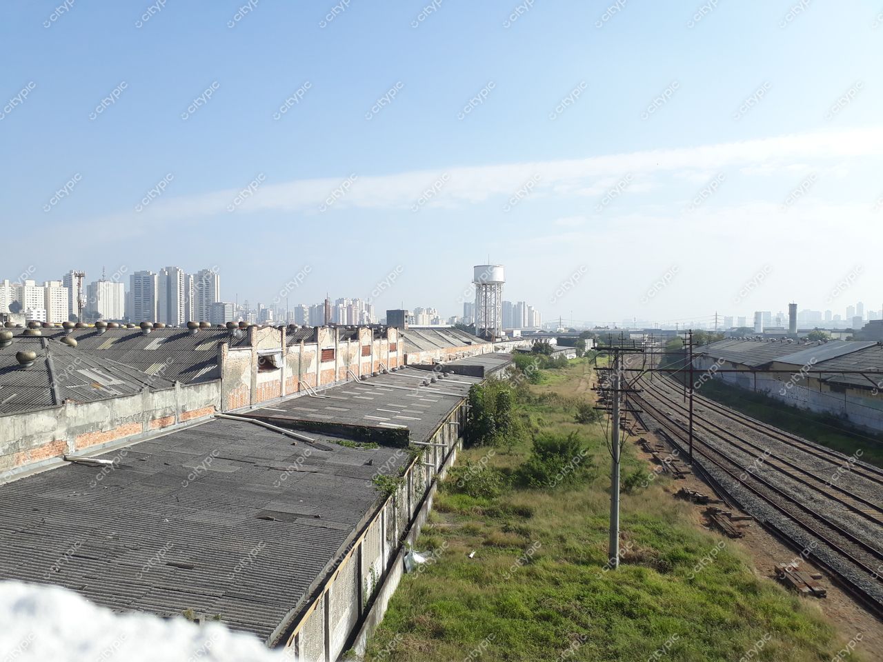 São Paulo, São Paulo, vista ampla de galpões industriais com telhados ondulados e skyline sob céu claro e iluminado