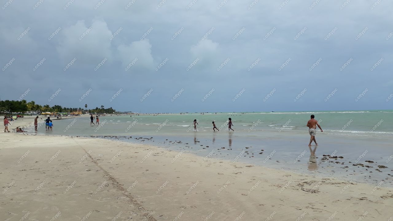 Paripueira, Alagoas em dia nublado com água verde calma e pessoas na areia e à beira d’água