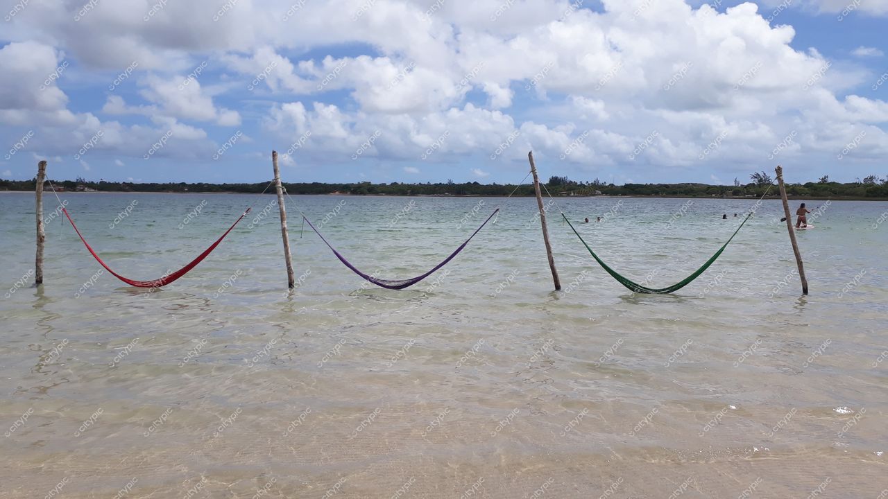Nísia Floresta, Rio Grande do Norte, redes coloridas na água rasa em dia parcialmente nublado com pessoas ao fundo