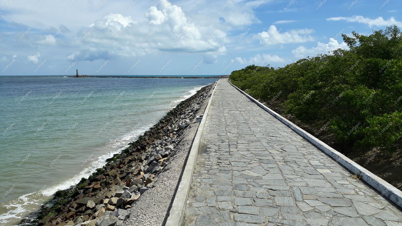 Natal, Rio Grande do Norte, calçadão à beira-mar com farol ao fundo e vegetação sob céu parcialmente nublado