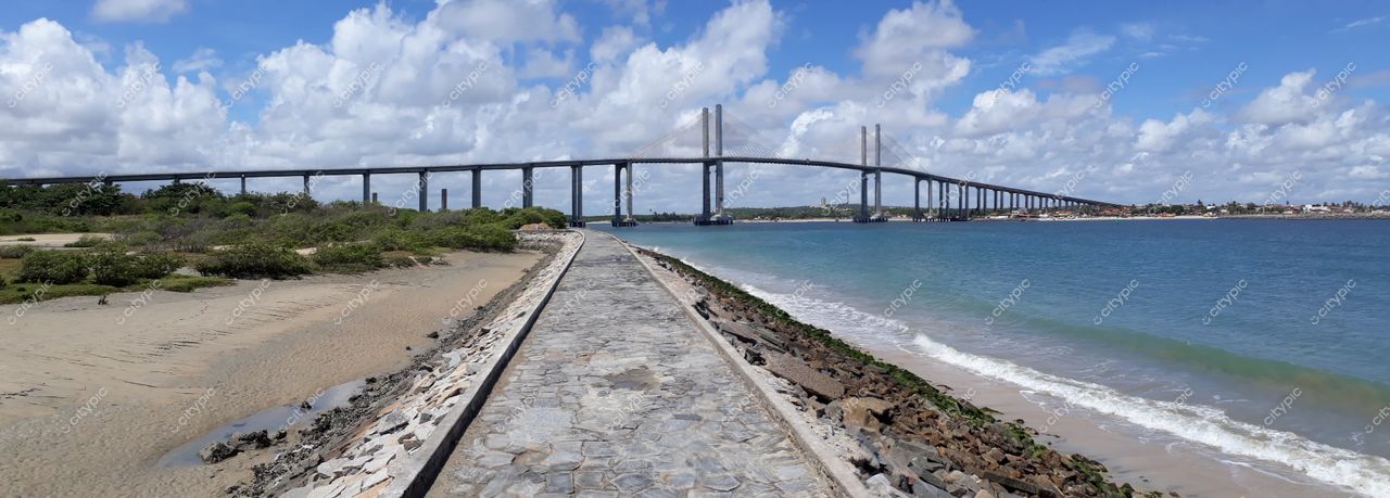 Natal, Rio Grande do Norte, ponte elevada sobre vegetação costeira com mar calmo e céu parcialmente nublado à tarde