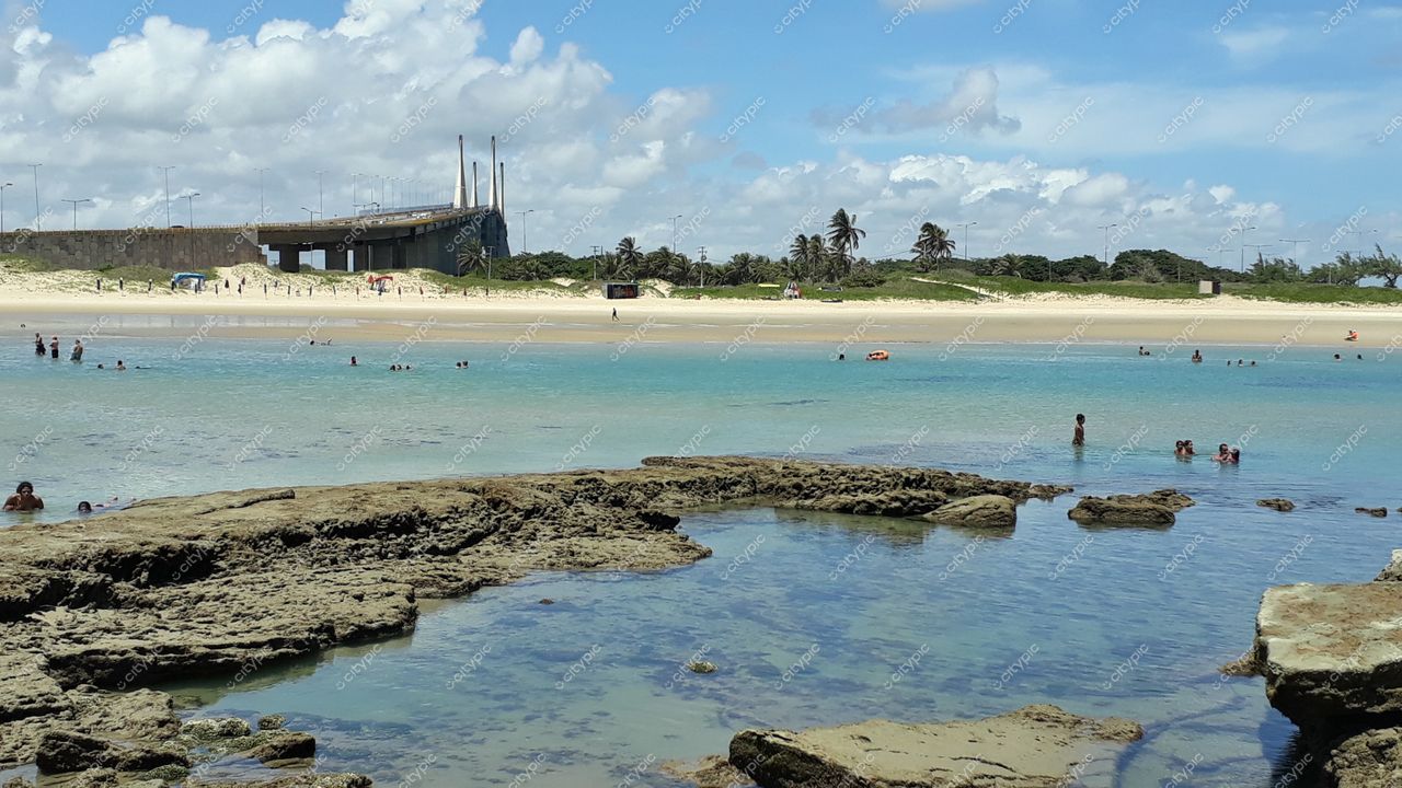 Natal, Rio Grande do Norte com praia de águas calmas, rochas visíveis e pessoas se divertindo sob céu parcialmente nublado