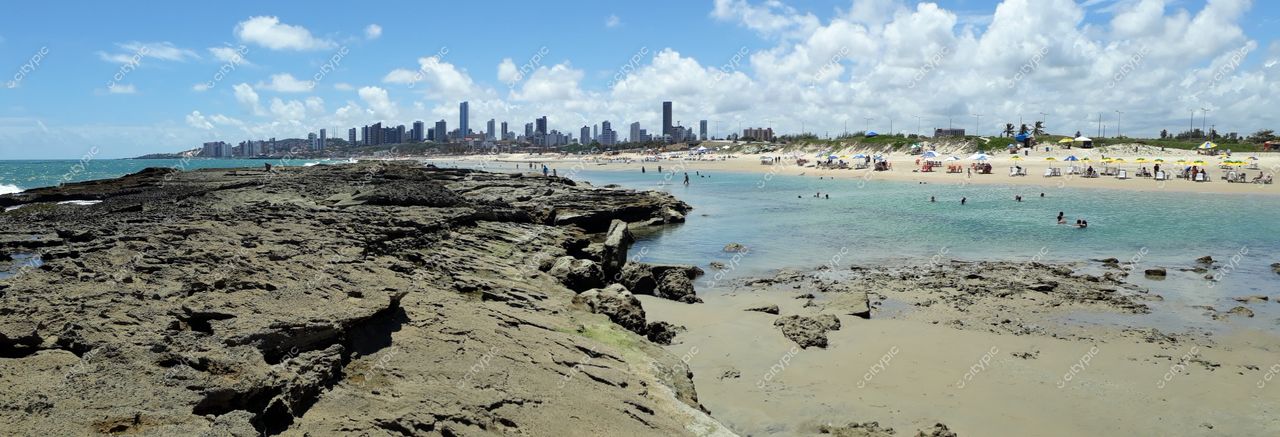 Natal, Rio Grande do Norte, vista panorâmica da praia com rochas, areia clara e silhueta urbana em tarde ensolarada