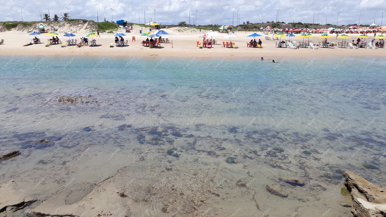 Natal, Rio Grande do Norte em dia ensolarado com cadeiras e mesas coloridas na praia e vegetação ao fundo