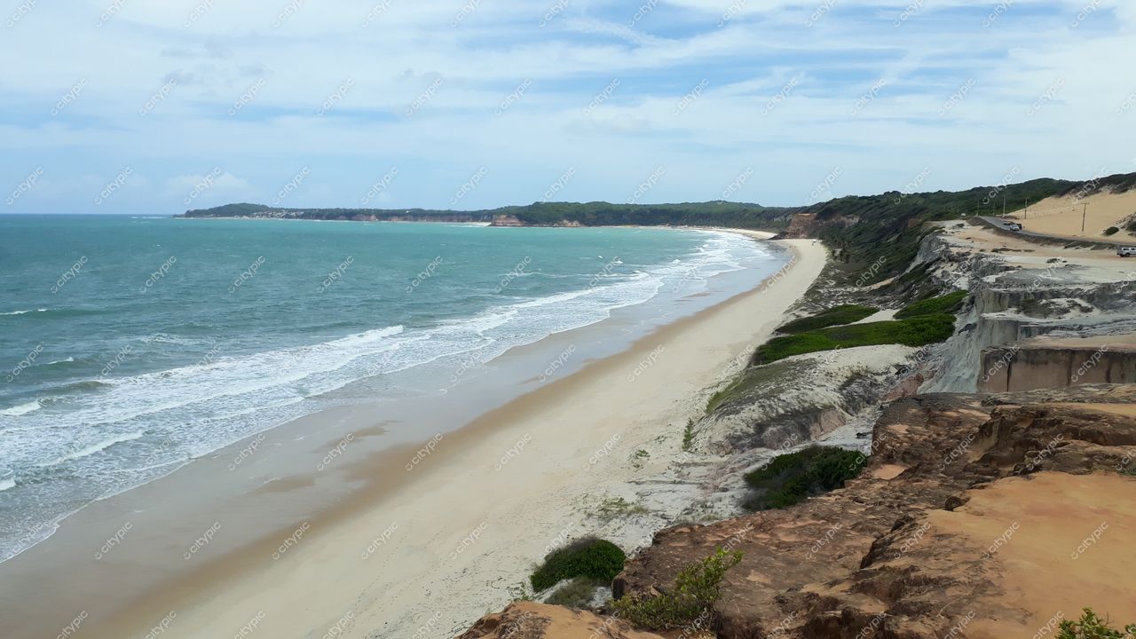 Tibau do Sul, Rio Grande do Norte com falésias de areia e vegetação verde sob céu nublado e mar em tons de azul