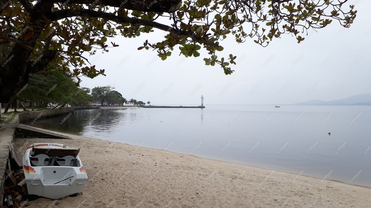 Ilha de Paquetá, Rio de Janeiro com praia clara, barco à beira da água e farol ao fundo em dia sereno