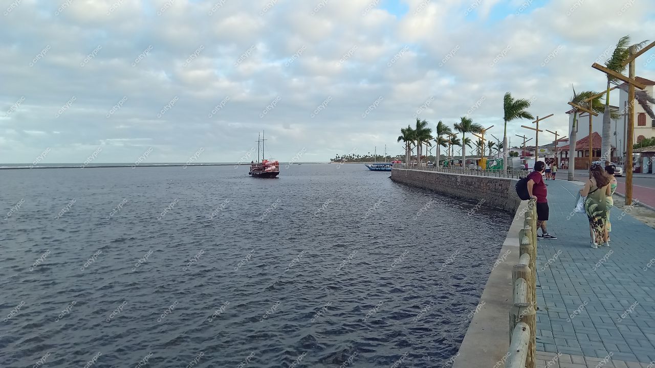 Orla de Porto Seguro em Porto Seguro com calçadão azul, palmeiras e barco ancorado sob céu nublado