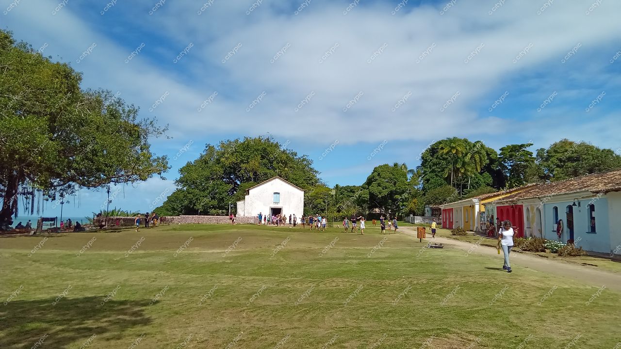 Centro Histórico de Porto Seguro em dia ensolarado com gramado verde, construções coloniais e visitantes explorando o local