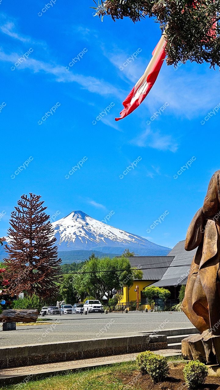 Vista diurna de um vulcão nevado com escultura de madeira e vegetação em calçada pavimentada e estacionamentos