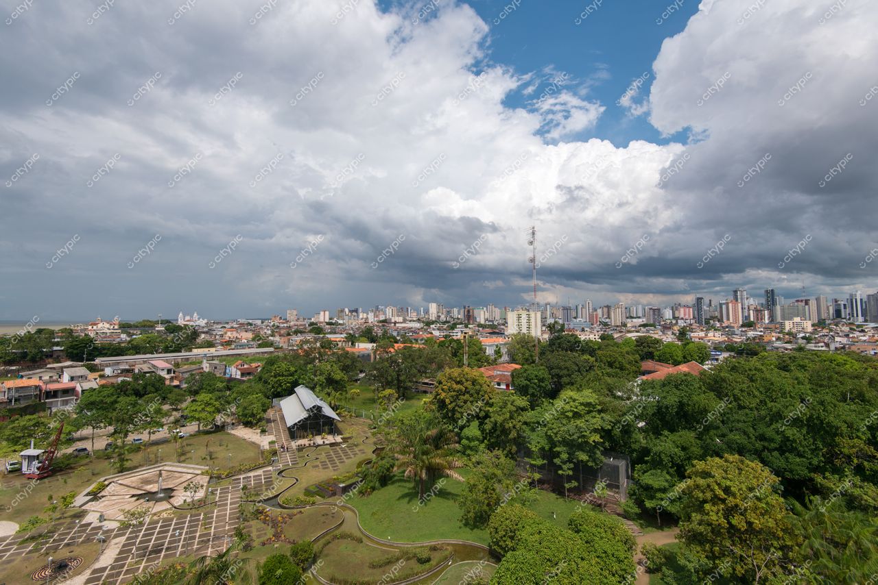 Belém, Pará com densa vegetação em primeiro plano e silhueta urbana sob céu parcialmente nublado ao fundo