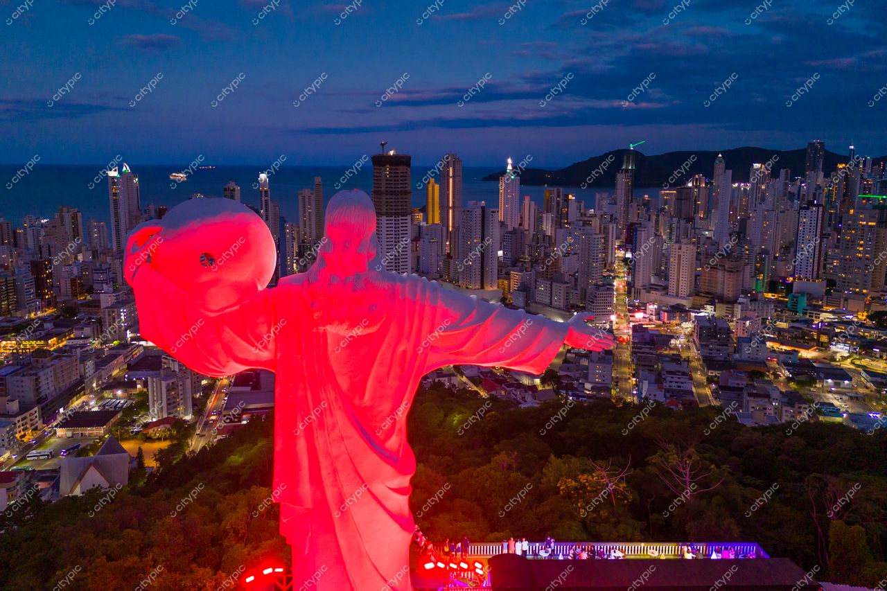 Balneário Camboriú, Santa Catarina, estátua do Cristo Luz iluminada em vermelho ao anoitecer com arranha-céus ao fundo