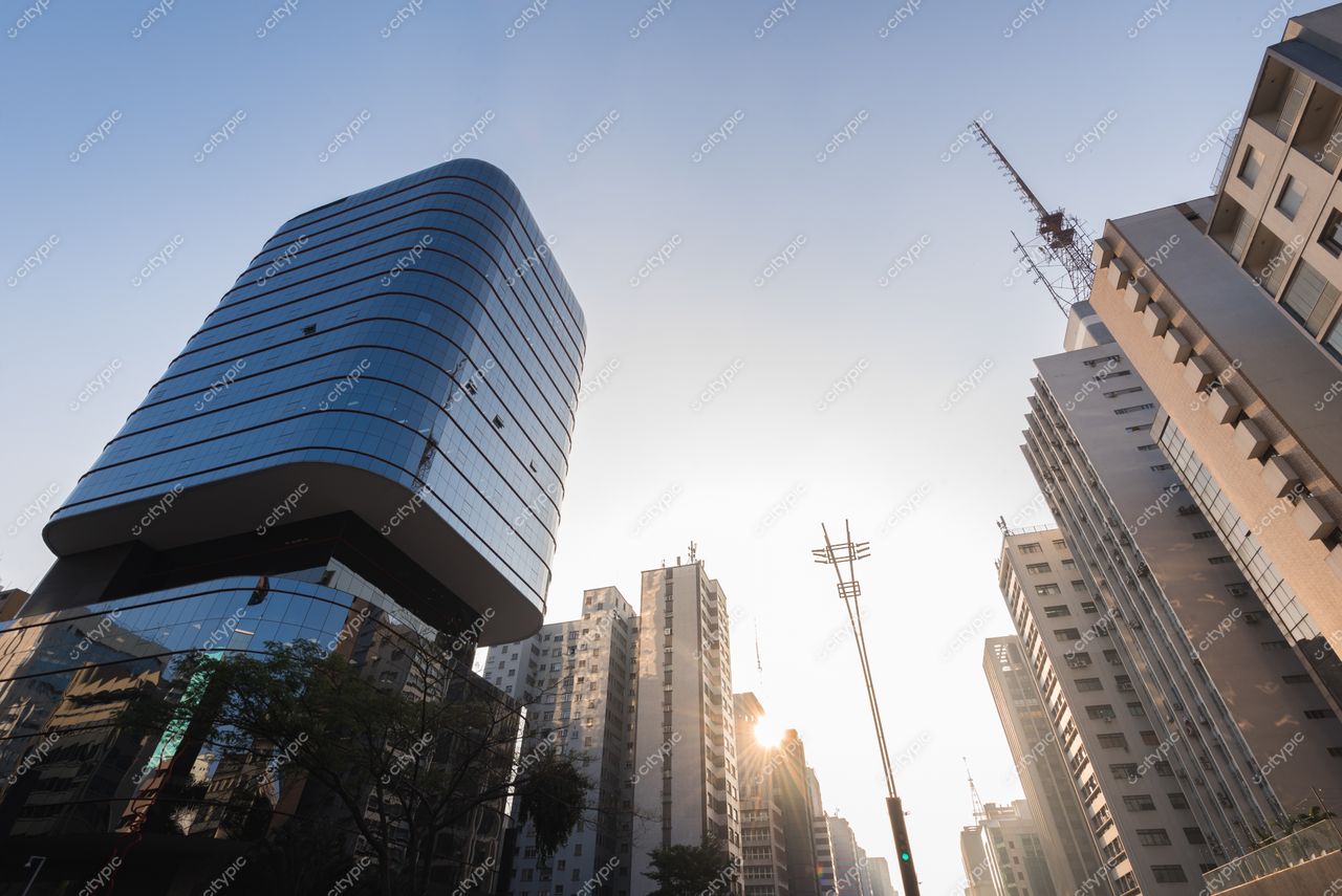 São Paulo, São Paulo, prédio moderno de vidro curvado ao amanhecer com vegetação e edifícios tradicionais ao fundo