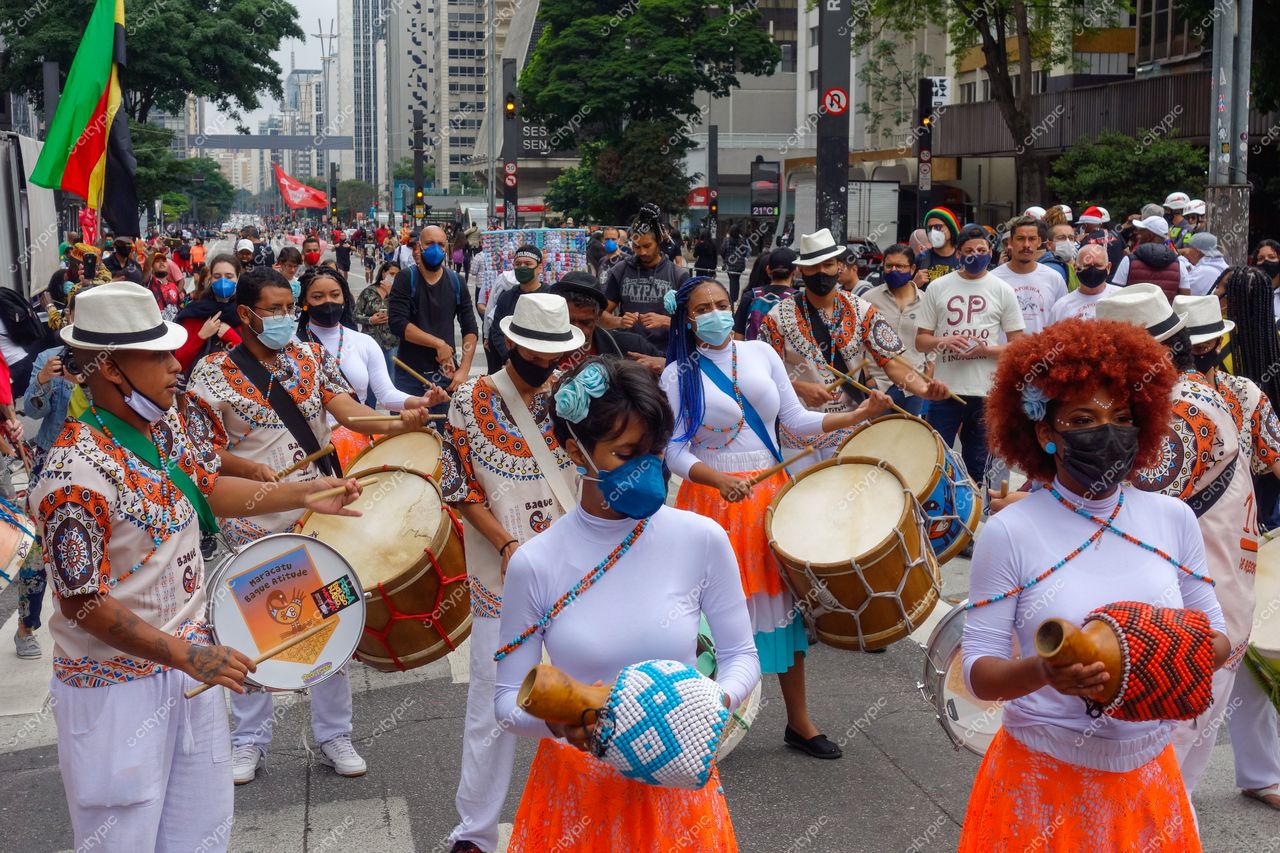 São Paulo, São Paulo, celebração de rua com pessoas em trajes coloridos e instrumentos musicais em ambiente urbano movimentado