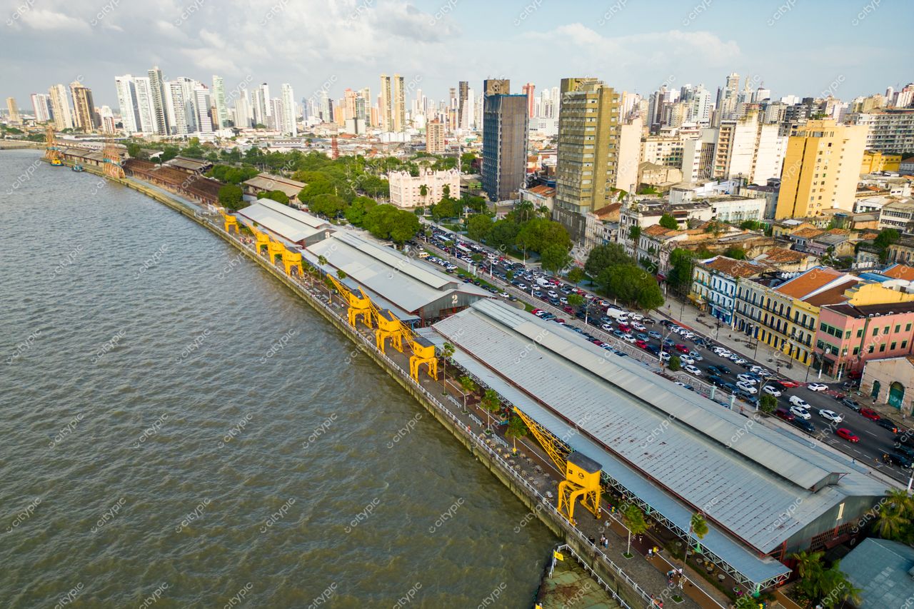 Belém, Pará vista aérea da orla com armazéns amarelos, vegetação nas margens e skyline urbano sob céu nublado