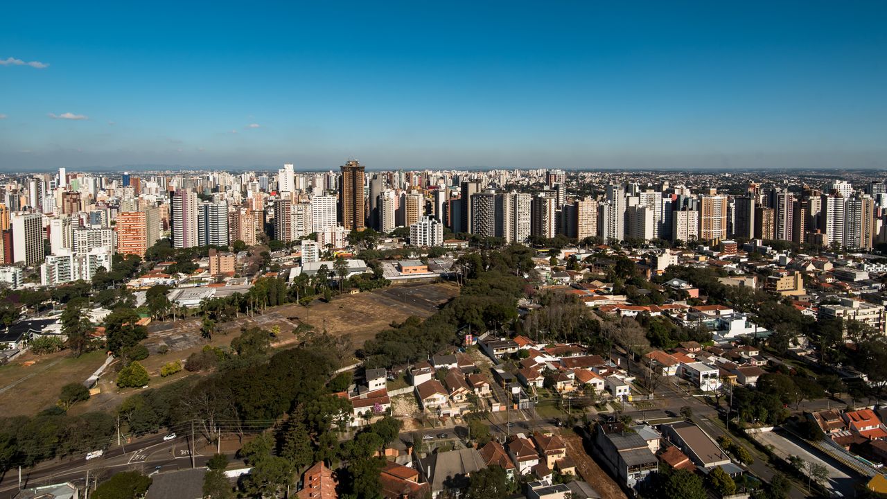 Curitiba, Paraná em dia ensolarado com arranha-céus modernos e áreas verdes contrastando na paisagem urbana